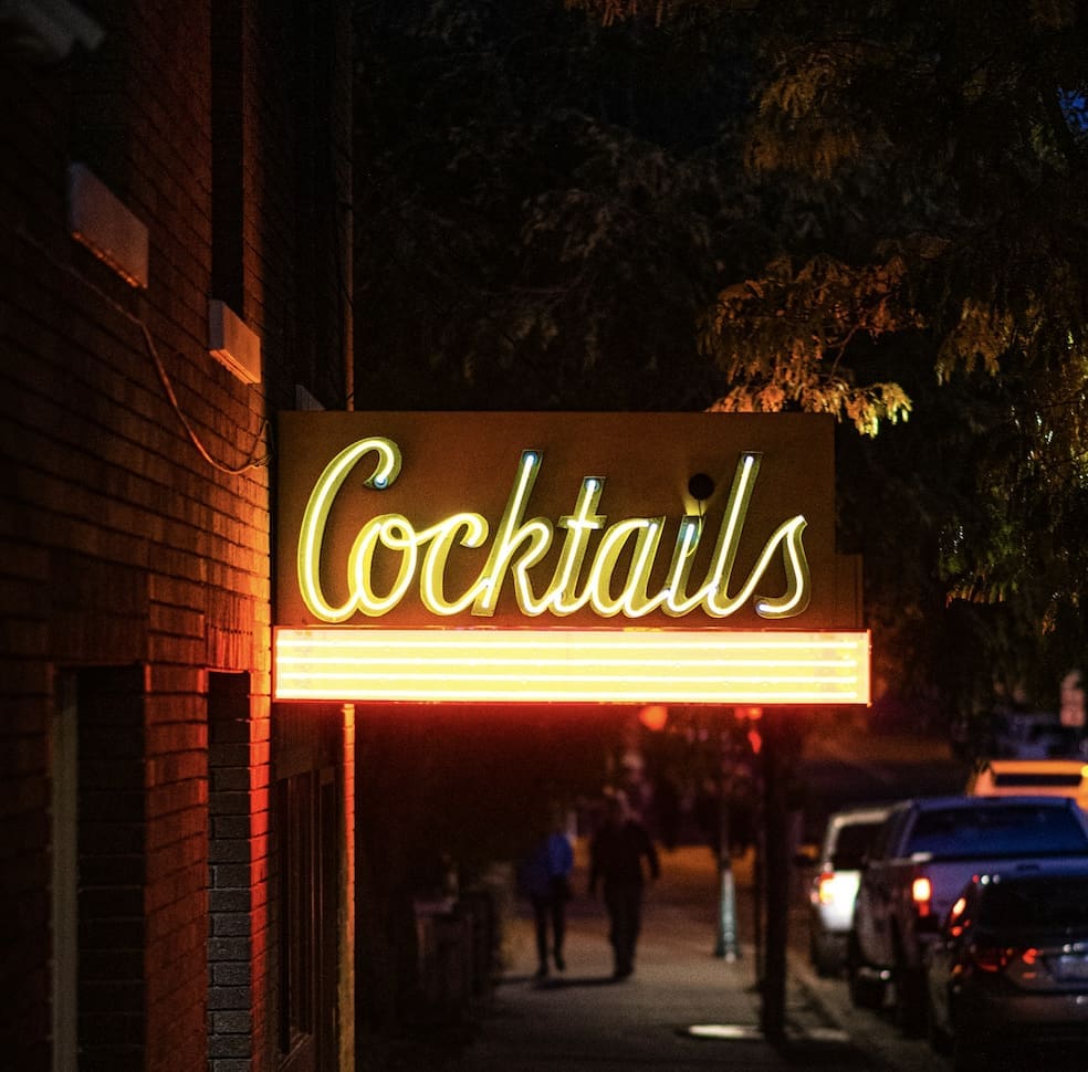 A street with a sign that says "Cocktails" lit up during the evening.